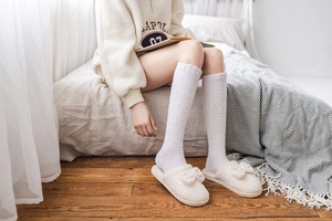 Close-up of soft white coral fleece knee-high socks and bow slippers for home comfort