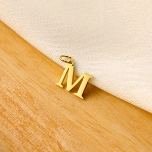 Macro detail of a golden letter M pendant on minimalist wood and fabric texture background