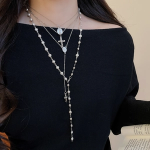 Detail of layered Y2K silver cross and pearl necklace set with a religious medal pendant