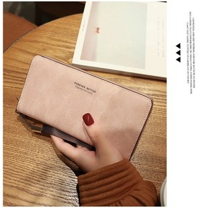 Pink long zipper wallet with wrist strap and embossed lettering in a lifestyle setting