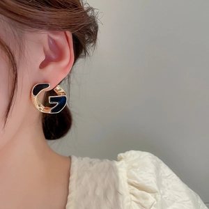 Close-up of golden metal earrings with black enamel in a stylish G letter design