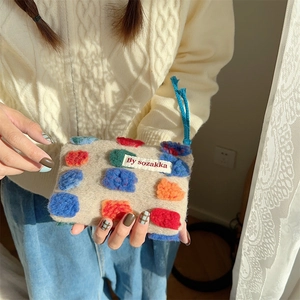 Detail of plush beige bucket bag featuring colorful tufted dots and brand label