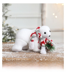 Close-up of white flocked polar bear figurine with a red scarf and holiday greenery