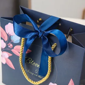 Navy floral gift paper bag with golden rope handles and a blue satin ribbon bow