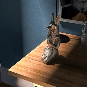 Artistic gold Anubis statue on a wooden desk with a textured blue wall backdrop