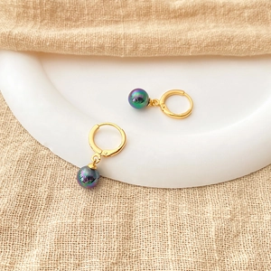 Detailed close-up of 18K gold-plated hoops with iridescent colorful pearls on beige linen