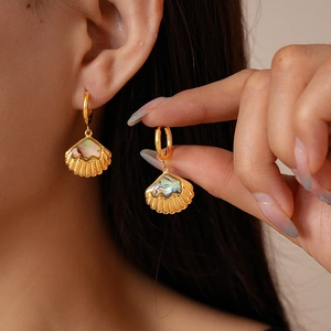 Golden fan-shaped shell earrings with rainbow abalone inlay worn by a female model