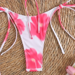 Close-up of floral bikini bottoms with side ties on a rustic straw mat background