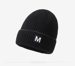 Detailed close-up of a black ribbed knit beanie featuring a stylish 'M' letter patch