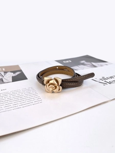Detail view of thin dark brown leather belt featuring a 3D gold camellia flower buckle