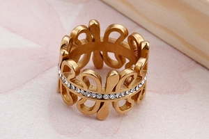 Detailed close-up of a wide hollow gold ring with inlaid rhinestones on a textured surface