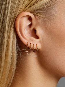 Close-up of four sizes of golden S925 sterling silver hoop earrings on ear lobe