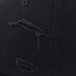 Macro shot of distressed black cotton fabric with vintage ripped hole detail on baseball cap
