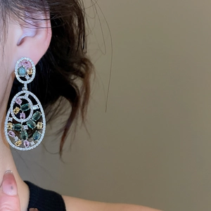 Close-up of elegant hollow oval earrings with colorful gemstones worn on the ear