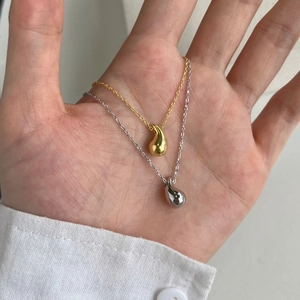 Detail of polished bean pendant necklaces in gold and silver held by a hand