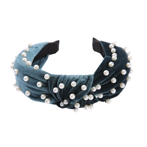 Close-up of a dark green velvet headband featuring a knotted design and white pearls