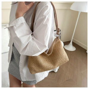 Close-up of handwoven straw tote bag with brown leather strap on a model's shoulder