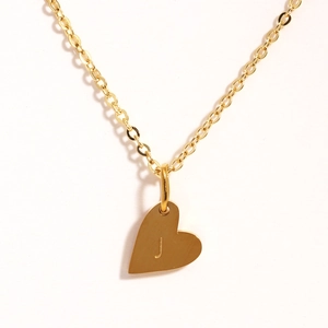 Détail d'un pendentif cœur doré avec gravure de la lettre J sur une chaîne en acier