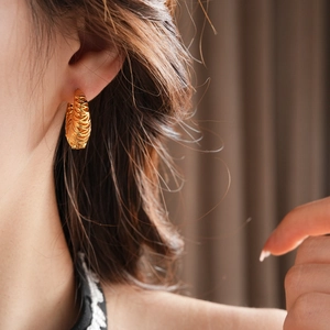 Close-up of 18k gold plated twisted hoop earring worn by a model in soft lighting