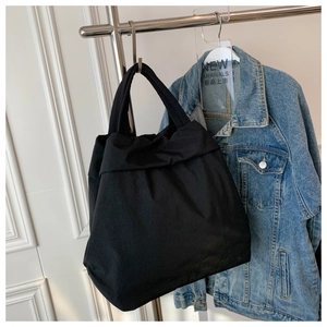 Detail of a large black canvas tote bag hanging on a metal hanger with a denim jacket