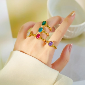 Detail of five gold-plated rings with colorful oval gemstones on a model's hand