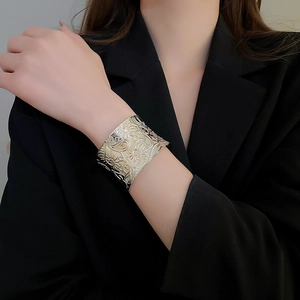 Macro detail of wide silver cuff bracelet with intricate floral engravings worn on wrist