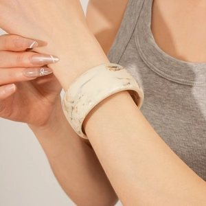 Detailed view of fashion wide marble-patterned resin bangle in cream white with brown swirl