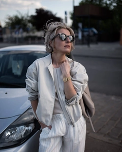 Detail of cream casual zip jacket and striped trousers styled with gold watch by a car