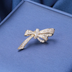 Macro shot of gold bow brooch with micro-pave zircons on a navy textured stand