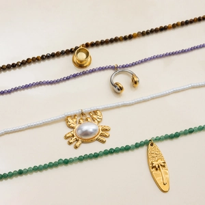 Flat lay of layered titanium steel beaded necklaces with gold and pearl pendants
