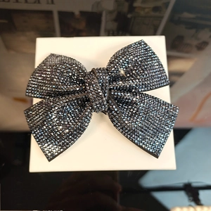 Detail view of a large black bow hair clip featuring sparkling rhinestones in a gift box