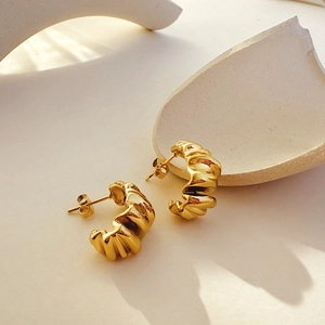 Macro detail of 18K gold croissant earrings showing textured pleats and polished metal