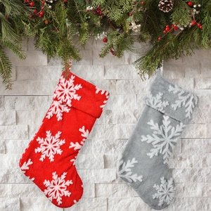 Plush red and grey Christmas stockings with white snowflake patterns on a wall