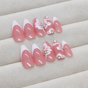Pink French almond press-on nails with white flower designs and sparkling rhinestones