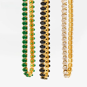 Detail of tennis bracelets with oval-cut green, black, and clear gemstones in gold finish