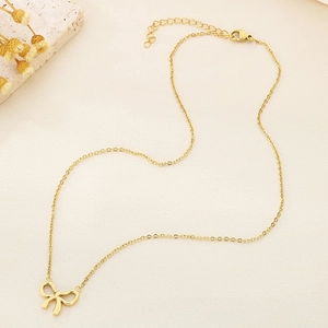 Close-up of golden bow pendant necklace with adjustable chain on beige texture