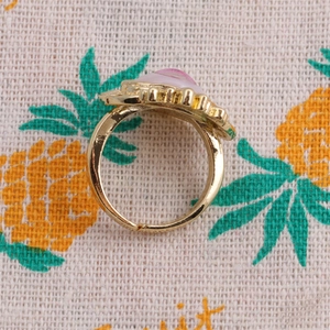 Detail of adjustable gold ring with pink and white zircon stones on a patterned fabric