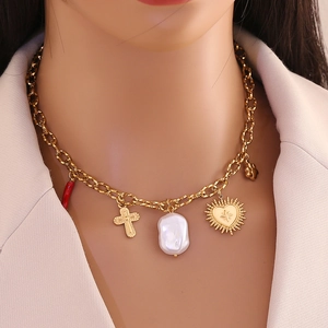 Gros plan du collier en acier doré avec croix, perle baroque et pendentifs en cœur