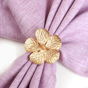 Close-up of golden flower napkin ring with brushed metal texture on purple linen cloth
