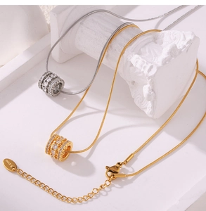 Detailed view of gold and silver cylinder pendants with zircon inlay on snake chains