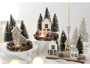 Close-up of wooden Christmas houses with snowy pine trees and pinecones on white fabric