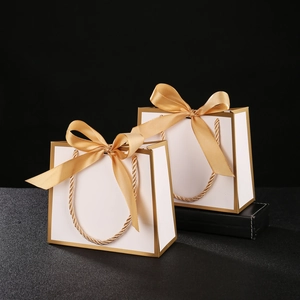 Close-up of elegant white gift bag with gold trim and a wide golden ribbon bow