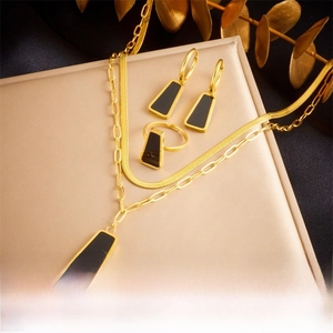 Close-up of gold layered chain necklace, earrings and ring set with black geometric inlays