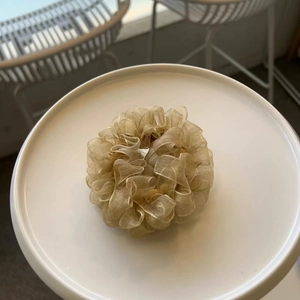 Detailed close-up of a golden pleated chiffon scrunchie placed on a white ceramic plate