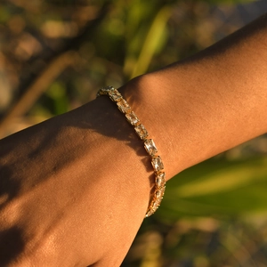 Detail of gold tennis bracelet with rectangular zircons worn on wrist in golden hour light