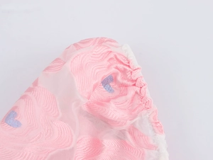 Detail of pink jacquard fabric with blue embroidered hearts and white sheer tulle sleeve