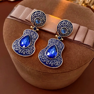 Dettaglio di orecchini vintage in smalto blu con motivi floreali su velluto