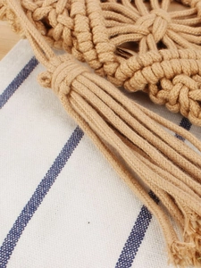 Handwoven khaki cotton rope beach bag with fringe tassels on blue striped background