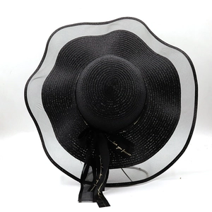 Détail de chapeau en paille noir avec bord ondulé en résille et nœud à lettres dorées