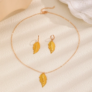Macro shot of gold leaf pendant necklace and matching earrings set on textured beige surface